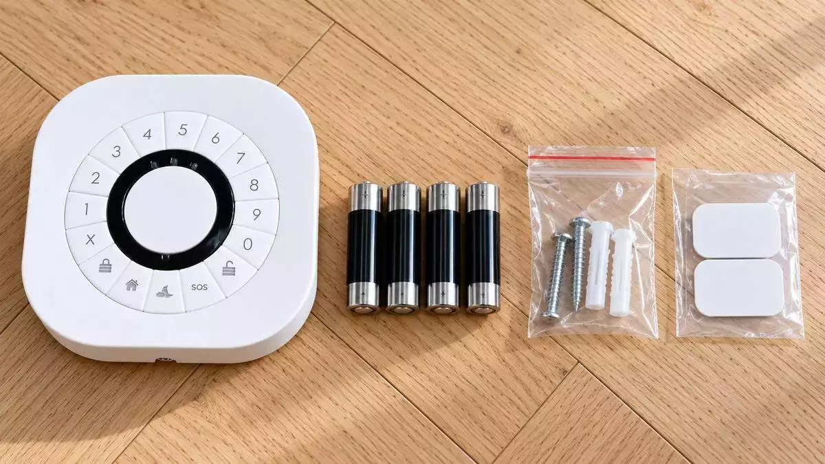 Clavier Zigbee frient accompagné de ses quatre piles AA, des vis et chevilles de fixation sur un parquet en bois clair.
